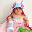 Baby wrapped in a pink hooded towel holding a bottle of MooGoo Bubbly Wash