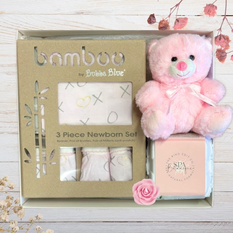Bamboo by Bubba Blue baby gift set with pink teddy bear, clothing, and Johnson's product in gift box on a wooden surface.