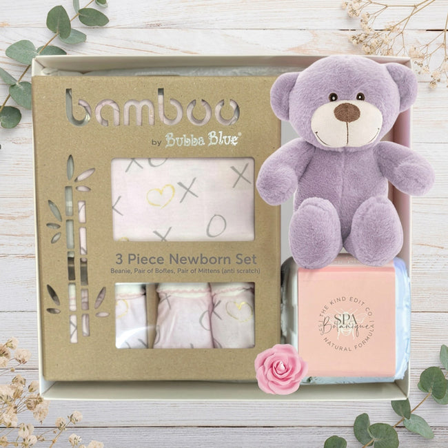 Bamboo by Bubba Blue baby gift set with purple teddy bear, clothing, and Johnson's product in gift box on a wooden surface.