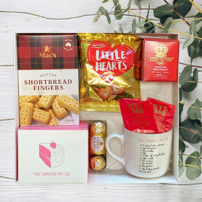 Gift set with cookies, tea, and a mug in gift box on a wooden surface with greenery.
