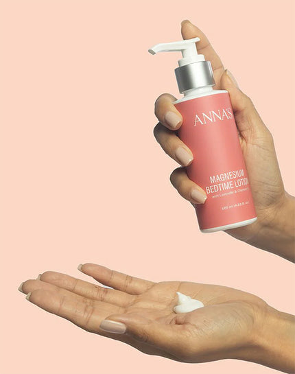 Hand holding a bottle of Anna's magnesium bedtime lotion with a small amount on the palm against a pink background