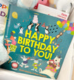 Children's book titled 'Happy Birthday To You' with animal illustrations on a white surface.