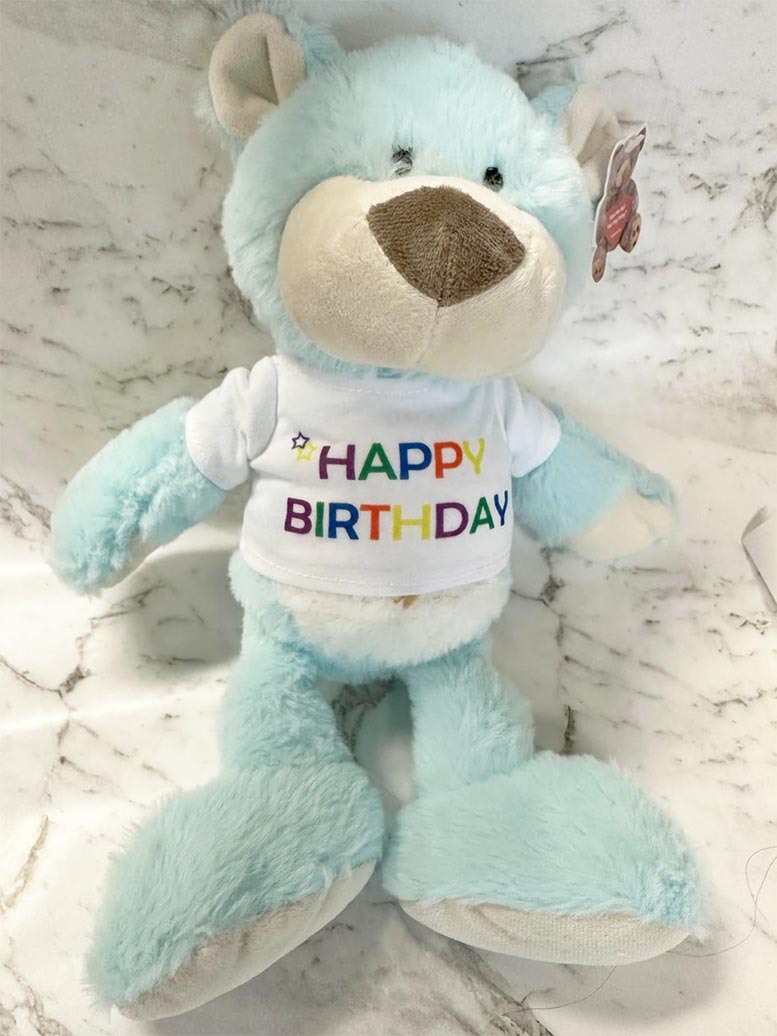 Light blue teddy bear with a 'Happy Birthday' shirt on a marble surface