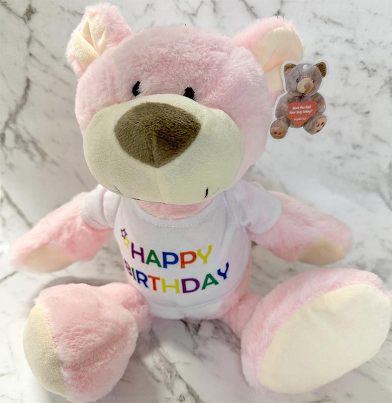 Pink teddy bear with a 'Happy Birthday' shirt on a marble surface