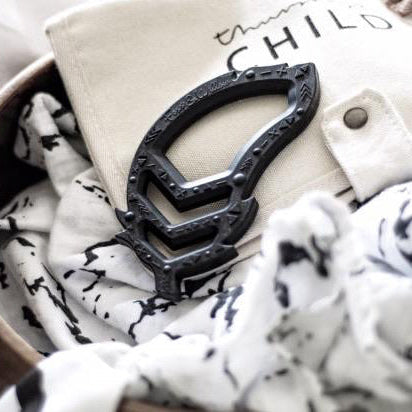 Black teether toy item on a textured surface with 'CHILD' text in the background