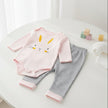 Baby outfit with pink and white striped onesie and gray pants on a table
