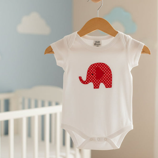 White baby onesie with a red polka dot elephant design in a baby nursery