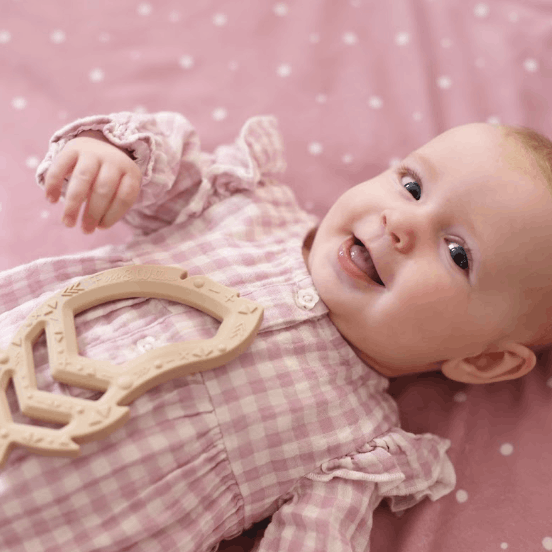 Baby girl with Feather Teether toy on pink blanket