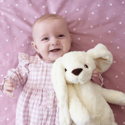 Baby girl holding white bunny on pink dotty blanket