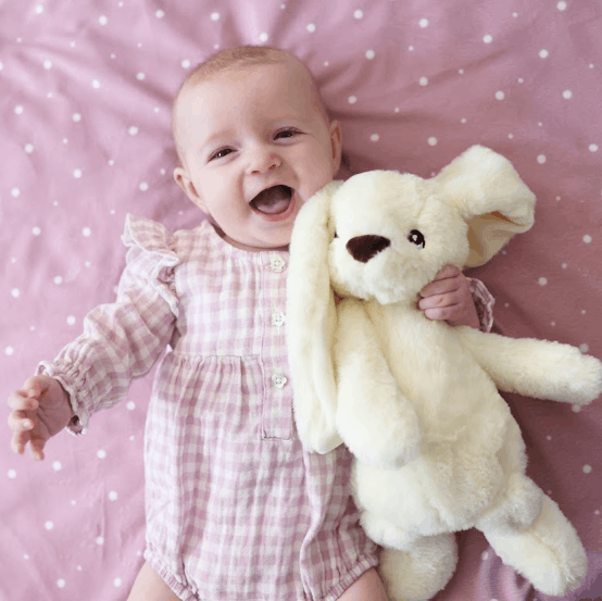 Baby girl holding white bunny on pink blanket