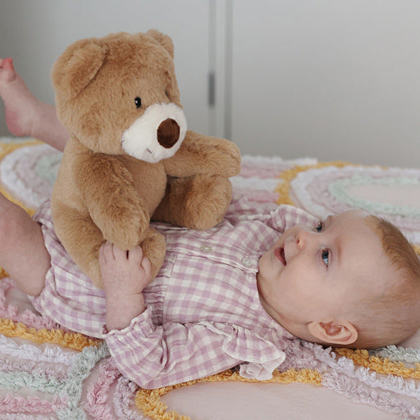 Baby laying on bed with brown bear