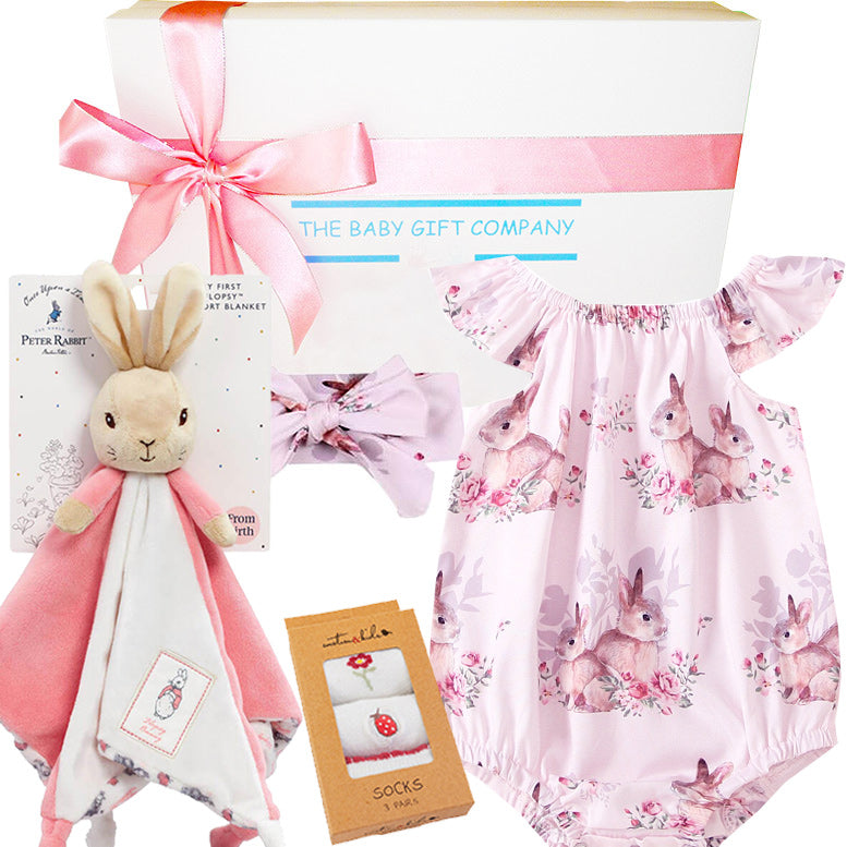 Baby gift set with pink bunny-themed romper, plush toy, headband, and socks from 'The Baby Gift Company'.