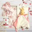 Beatrix potter Baby gift set with floral outfit, plush flopsy toy, and sock in gift box on a wooden surface.