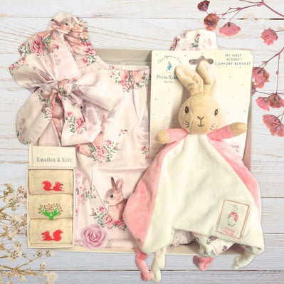 Beatrix potter Baby gift set with floral outfit, plush flopsy toy, and sock in gift box on a wooden surface.