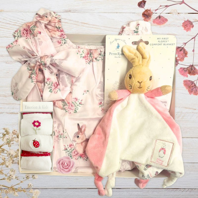 Beatrix potter Baby gift set with floral outfit, plush flopsy toy, and sock in gift box on a wooden surface.