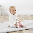 Baby sitting on a rug holding a plush Beatrix Potter Flopsy toy in a room with a light-colored floor.