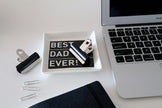 Laptop on a desk with 'Best Dad Ever' coin dish and office supplies