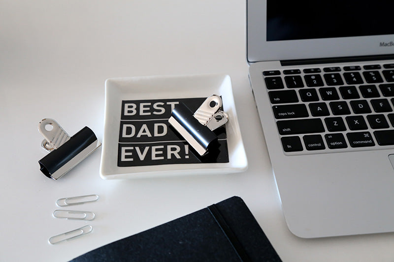 Laptop on a desk with 'Best Dad Ever' coin dish and office supplies