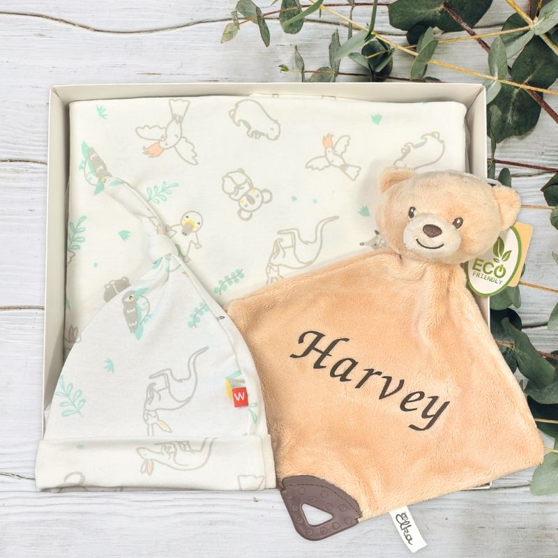 Baby comfort blanket and teddy bear with 'Harvey' embroidered, in a box with greenery around.
