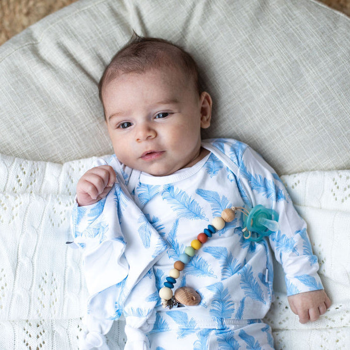 baby laying on blanket and wearing blue feather outfit and dummy