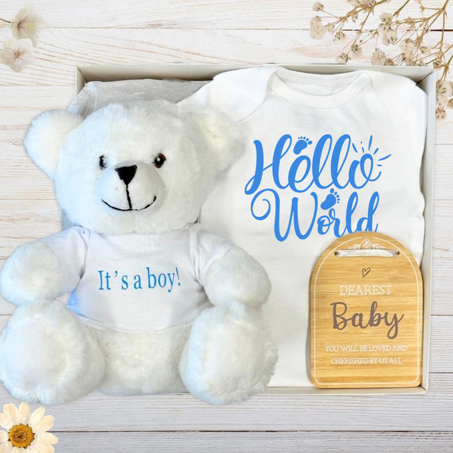 Beautifully presented Baby Gender Reveal Gift Hamper with its a boy white teddy bear and Hello world baby clothes on a wooden surface.