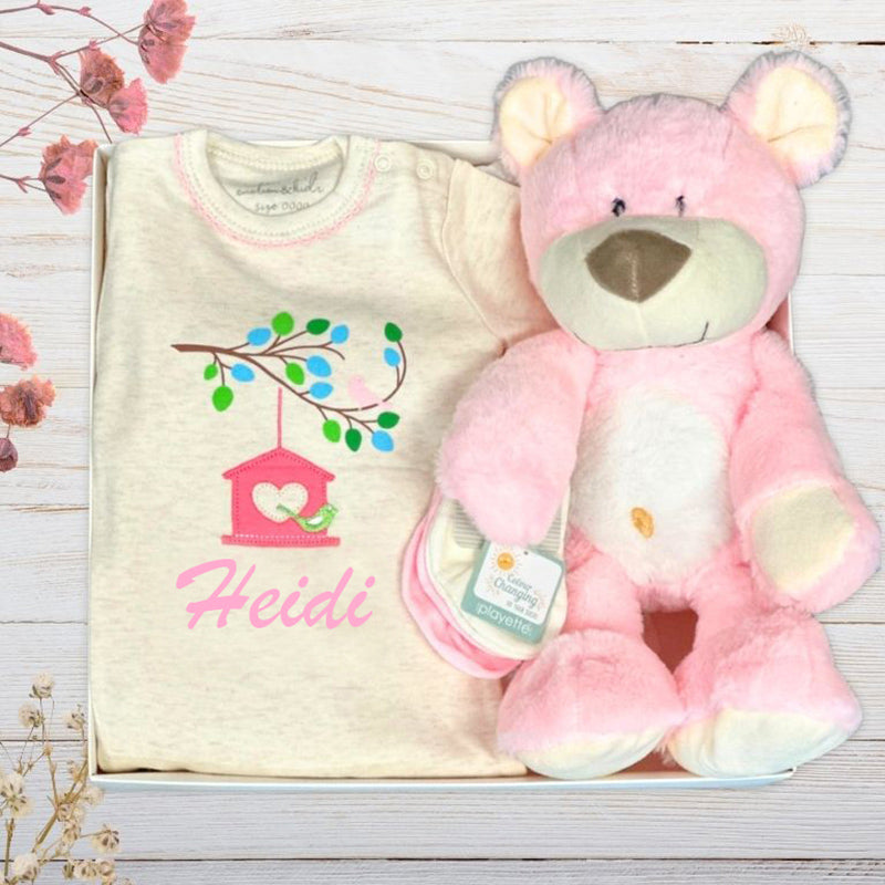 Baby outfit with embroidered design and pink teddy bear on a wooden surface.