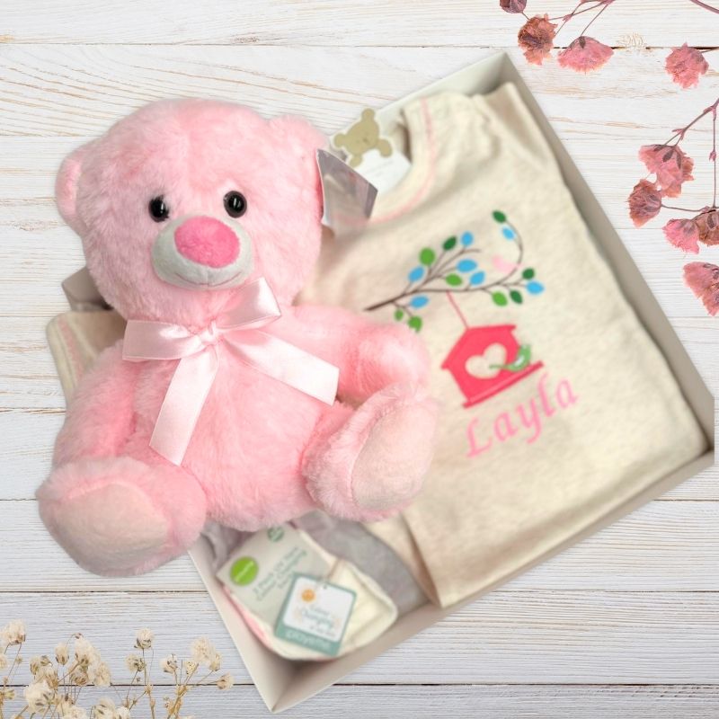 Baby outfit with embroidered Layla name and pink teddy bear on a wooden surface.