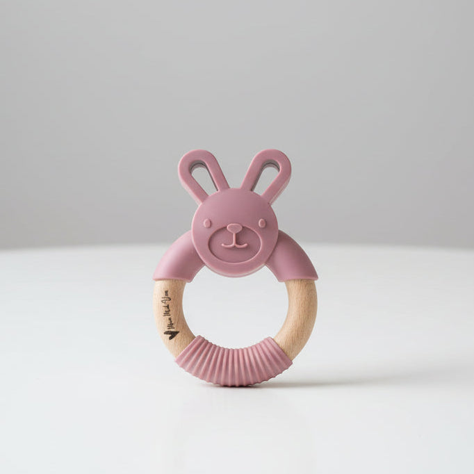 Pink bunny-shaped teething ring with wooden ring on a table background