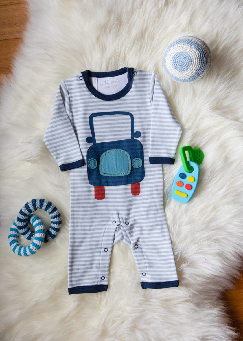 Striped baby romper with car design on a fluffy white surface with toys around