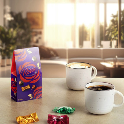 Cadbury Roses chocolate packaging with two mugs of coffee on a table.