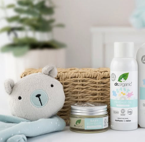 Dr. Organic baby products including a bottle, jar, and plush toy on a white surface with a blurred plant in the background.
