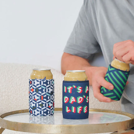 Person holding a can with a colorful sleeve labeled 'It's a Dad's Life' on a table.