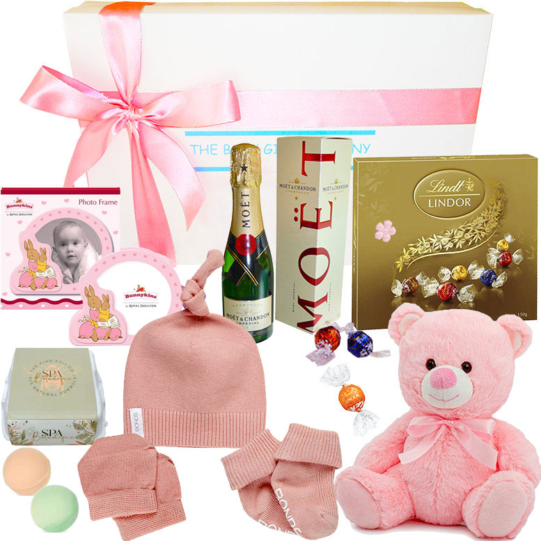 Baby gift set with pink teddy bear, champagne, Lindt chocolate, and baby items on a white background