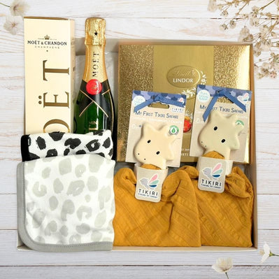 Baby Gift box with Moët & Chandon champagne, plush giraffe toys, and baby bibs on a wooden surface.