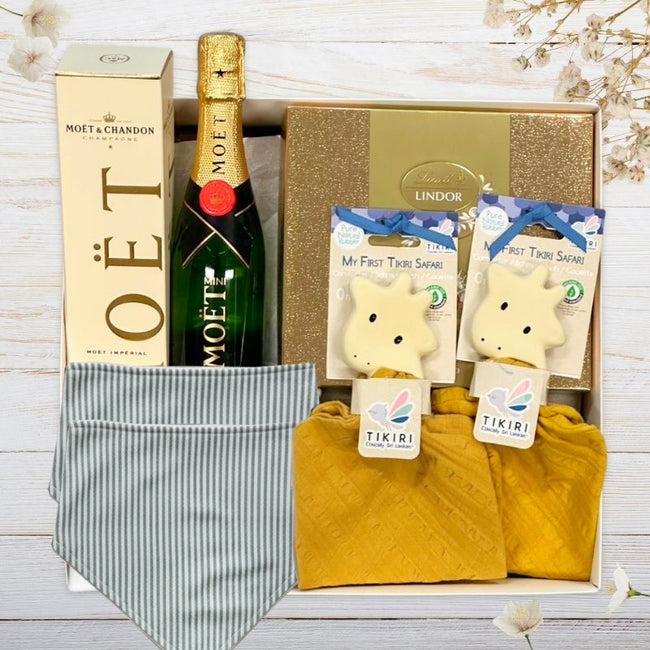 Baby Gift box with Moët & Chandon champagne, plush giraffe toys, and baby bibs with stripes on a wooden surface.