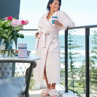 Woman in a pink robe holding a coffee cup on a balcony with ocean view
