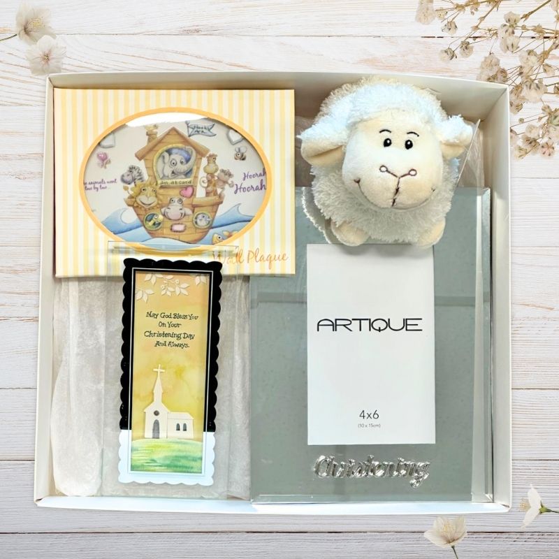 Gift set with christening photo frame, card, and plush lamb toy in a baby gift box on a wooden surface.