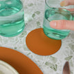 Green glass with a hand holding it on a textured surface with an orange coaster.