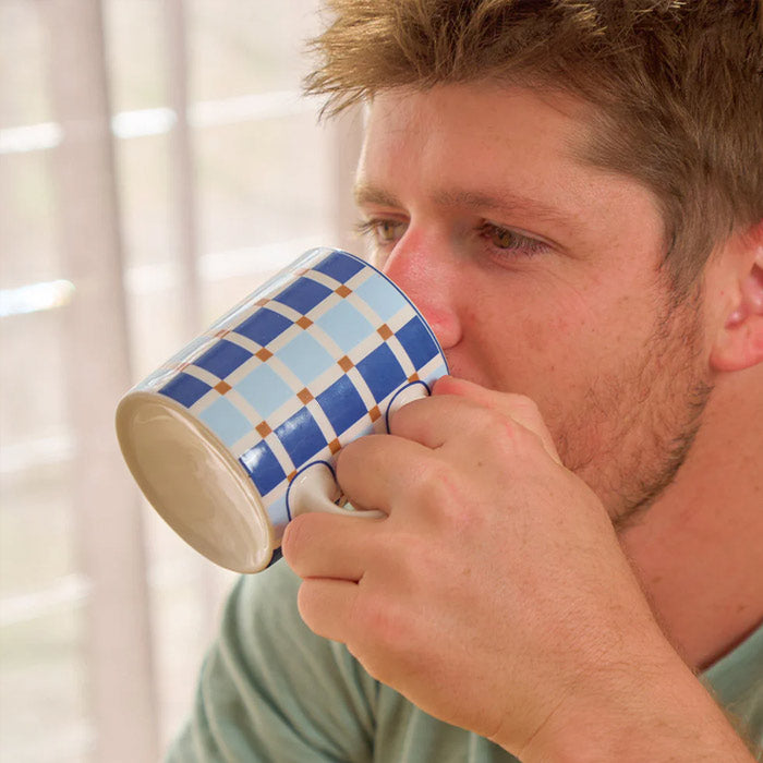 Man drinking from a blue and white checkered mug indoors