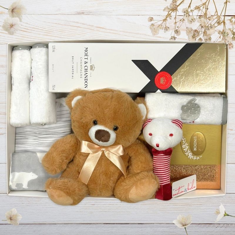 Gift set with teddy bear, baby clothes, and small plush toy in a box with Moét & Chandon branding.