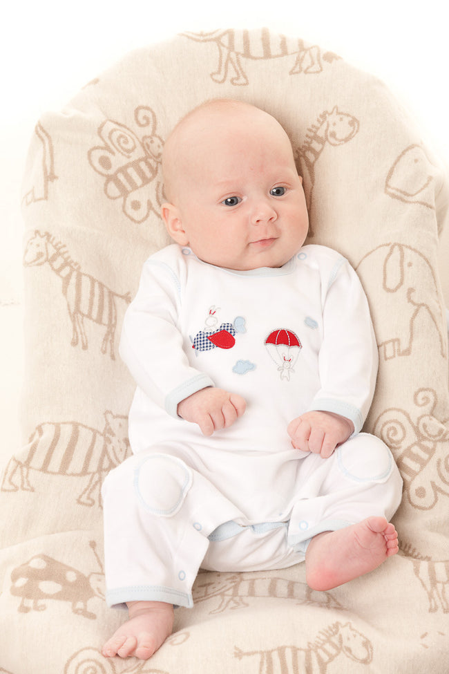 Baby in a white onesie with colorful designs sitting on a patterned chair.
