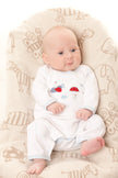 Baby in a white onesie with colorful designs sitting on a patterned chair.