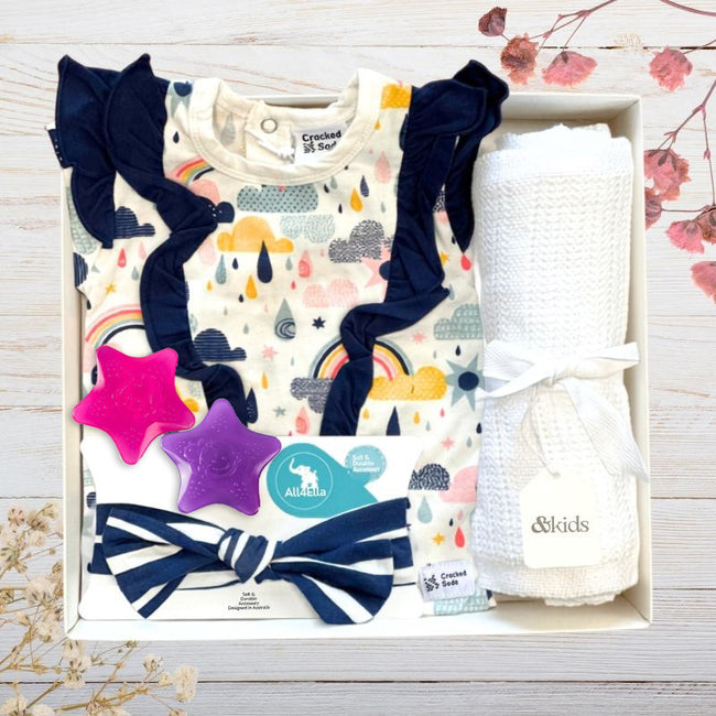 Baby gift set with onesie, headbands, star water teethers and blanket in a baby gift box on a wooden surface.