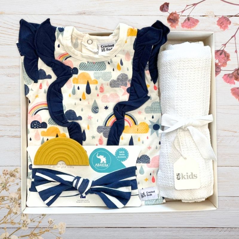 Baby gift set with onesie, headbands, and blanket in a baby gift box on a wooden surface.