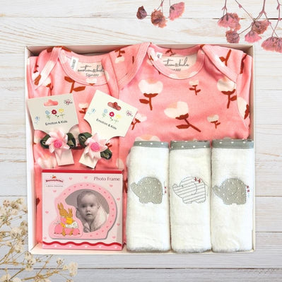 Baby gift set with clothes, bibs, and photo frame in gift box on a wooden surface