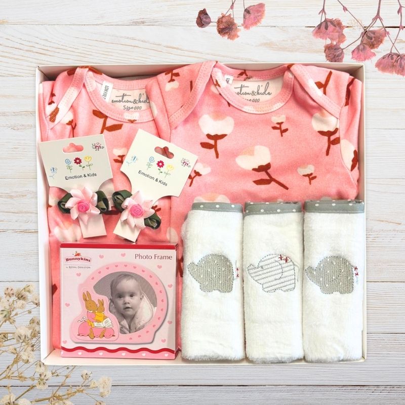 Baby gift set with clothes, bibs, and photo frame in gift box on a wooden surface