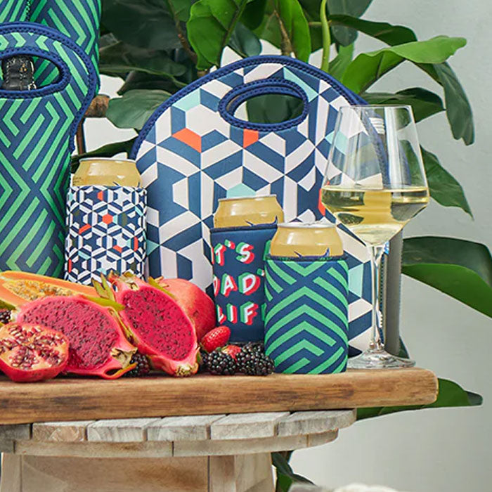 Colorful geometric-patterned can coolers with drinks and pomegranates on a table.