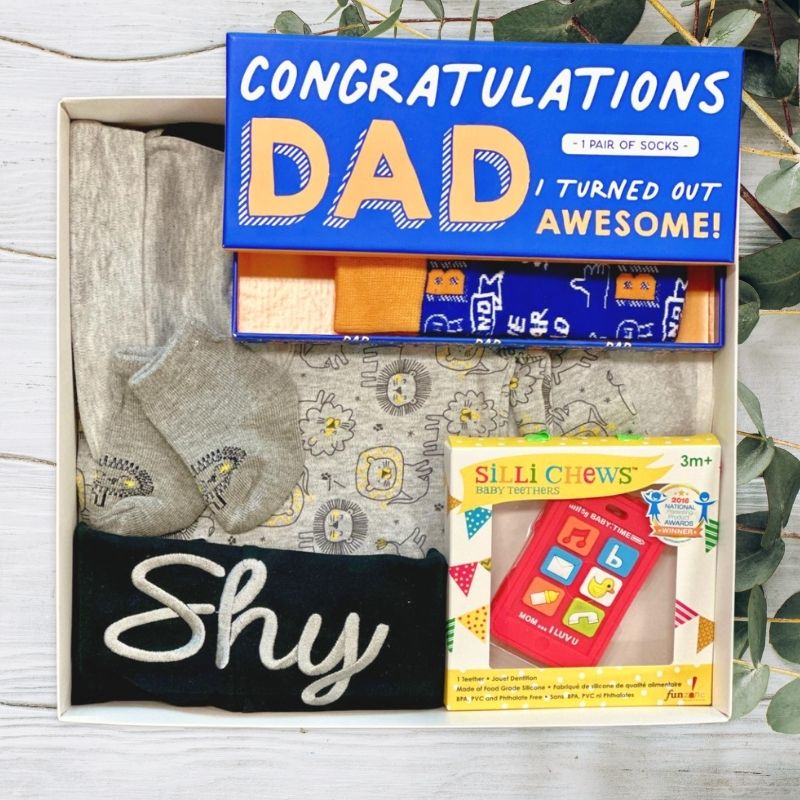 Baby Gift set for a father with socks, baby clothing, and toy on a wooden surface.
