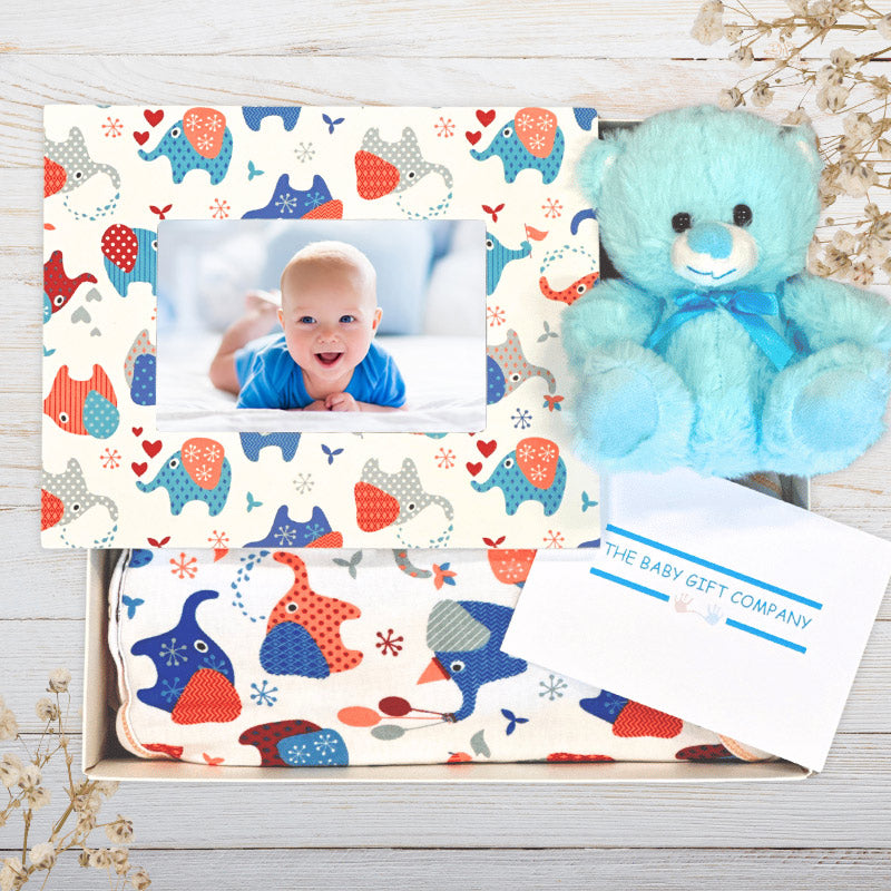 Baby gift set with teddy bear, photo frame, and blanket featuring animal patterns on a wooden surface.