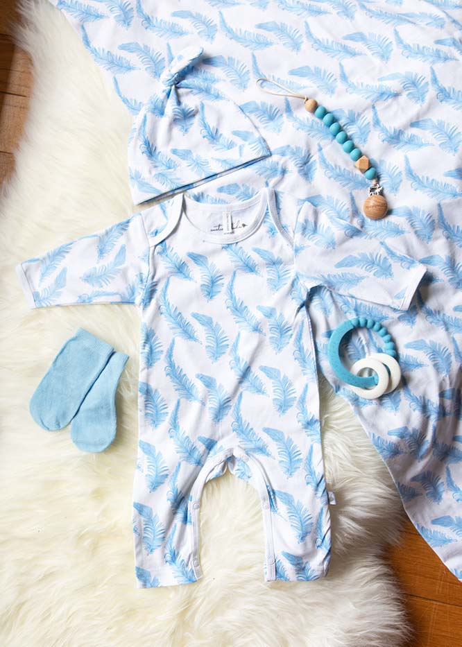 Baby onesie with blue and white pattern, socks, and teething ring on a soft surface